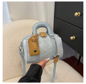 Detail of blue textured Boston handbag featuring debossed logo and metal chain charm