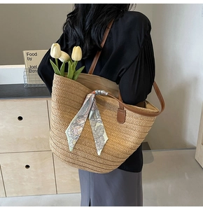 Detail of woven straw tote bag with brown leather straps and colorful floral silk scarf