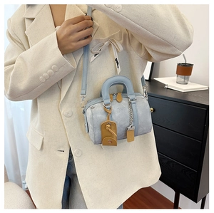 Detailed shot of a light blue cylinder handbag with tan accents and a metal chain detail