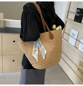 Close-up of woven straw tote bag with brown leather straps and decorative floral silk scarf