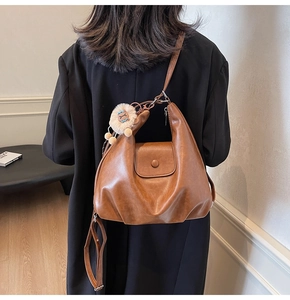 Detail of brown pleated crescent shoulder bag with lion plush charm on a model's shoulder