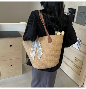 Detail view of woven straw tote bag with brown leather straps and floral silk scarf accessory