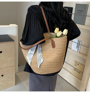 Detail of woven straw tote bag with brown leather handles and a blue printed silk scarf