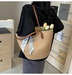 Detail of woven straw tote bag with brown leather handles and a blue floral scarf accent