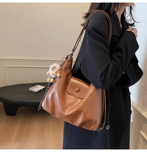 Detailed side view of brown faux leather tote bag with flap pocket and plush charm