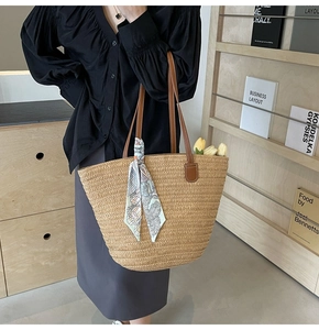 Detail of straw woven tote bag with brown leather straps and colorful floral silk scarf