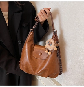 Brown retro oversized tote bag with plush lion charm and striped cord detail worn by model