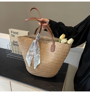 Close-up of woven straw tote bag with brown leather handles and decorative floral silk scarf