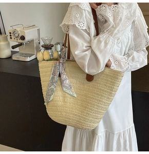 Detail of straw woven tote bag with leather handles and decorative floral silk scarf