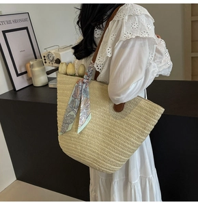 Detail of large straw tote bag with brown leather handles and decorative silk scarf