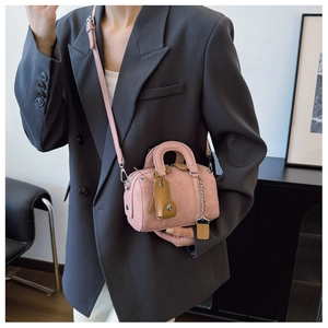 Pink matte Boston bag with round handles and metal chain detail on grey blazer