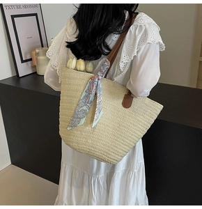 Detail of woven straw tote bag with brown leather handles and a blue floral scarf decor
