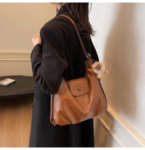 Detail of a brown leather hobo bag with flap magnetic closure and cute lion charm detail