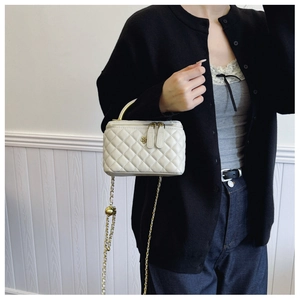 Detail of white quilted leather bucket bag with gold flower buckle and chain strap