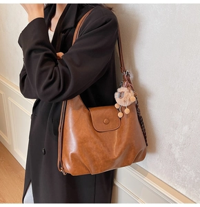 Brown vintage faux leather tote bag detail with cute lion charm worn over black coat