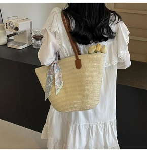 Close-up of straw tote bag with brown leather handles and decorative silk scarf