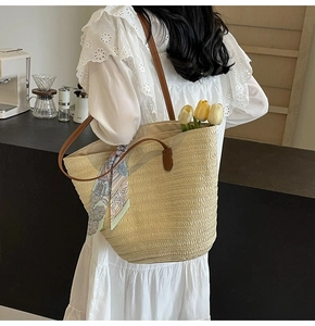 Detail of straw tote bag with brown leather straps and blue geometric print scarf accessory