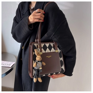 Detail of checkered tote bag with brown leather trim and a cute rabbit charm accessory