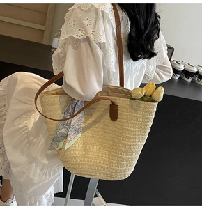 Detail of beige straw tote bag with brown leather straps and a decorative silk scarf