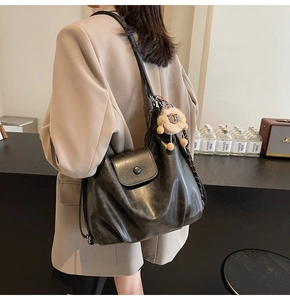 Detail of a large dark grey soft leather tote bag with a plush lion charm on shoulder strap