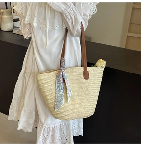 Detail of hand-woven straw tote bag featuring brown leather straps and silk scarf ornament