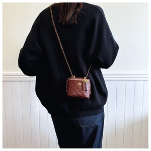 Brown quilted mini bucket bag with gold flower detail and chain strap worn by model