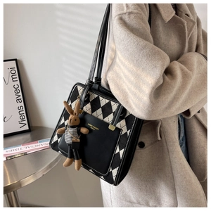 Detail of checkered canvas tote bag with leather pocket and cute rabbit charm on a beige coat
