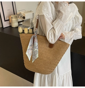 Detail of woven straw tote bag with brown leather handles and a blue printed silk scarf