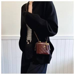 Detail of burgundy quilted leather mini bag featuring gold chain and floral pendant