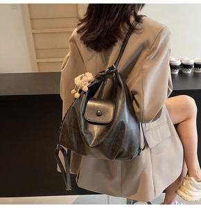 Detail of black faux leather backpack with plush pendant on a khakis blazer model