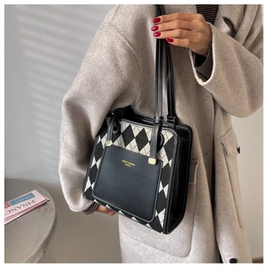 Detail of checkered tote bag with leather pocket and branding against sunlit wall