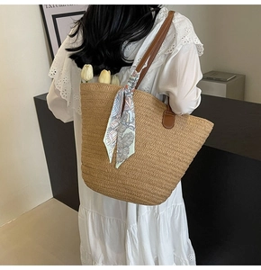 Detail of hand-woven straw tote bag with brown leather handles and decorative silk scarf