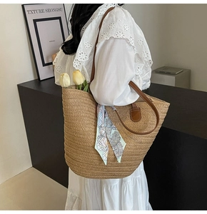 Detail of straw woven tote bag with brown leather handles and decorative silk scarf