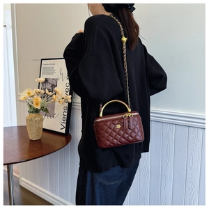 Detail of burgundy quilted leather bucket bag with gold flower emblem and metal handle