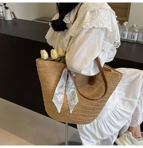 Large straw tote bag with floral scarf detail and brown leather straps worn on shoulder