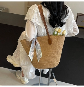 Detail of straw woven tote with floral scarf and leather handles on lace dress