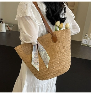 Detail of straw woven tote bag with brown leather handles and decorative floral silk scarf
