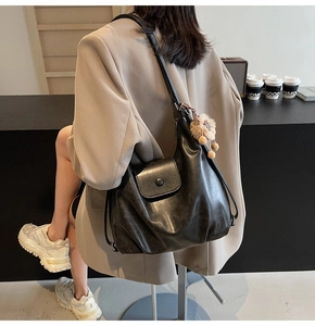 Detail of black leather tote bag with round button flap and beige plush pom-pom charm