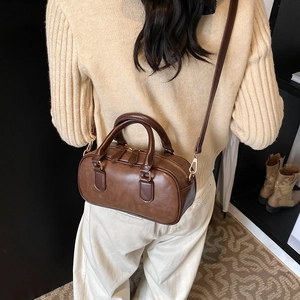 Deep brown matte Boston bag with double handles and gold hardware shown on a model