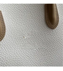 Gros plan sur le sac cabas en cuir grainé blanc avec logo doré et bordure marron