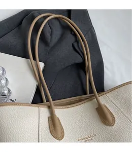 Gros plan d'un sac cabas en cuir grainé crème avec logo doré et fines bandoulières en cuir