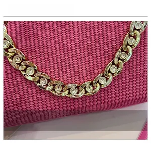 Close-up of pink woven handbag featuring a chunky gold chain strap with inlaid crystals