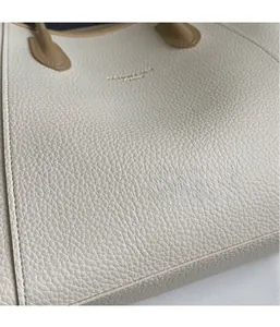Gros plan sur la texture du cuir grainé beige et le logo doré embossé du sac cabas