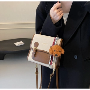 Detail of vintage beige and brown messenger bag with plush teddy charm and ribbon