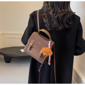 Detail of brown leather backpack featuring dual straps and a plush teddy bear charm