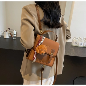 Side view of a vintage brown leather backpack with teddy charm and silk scarf handle