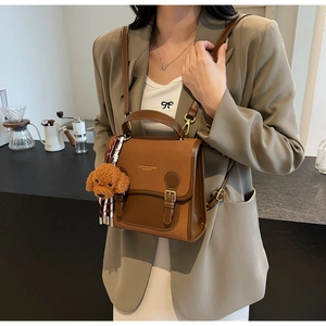 Detailed view of a brown vintage leather backpack featuring a cute teddy bear charm
