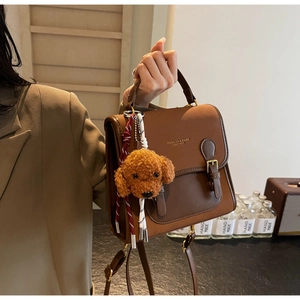 Brown leather crossbody bag detail featuring a cute teddy bear plush charm and metal buckle