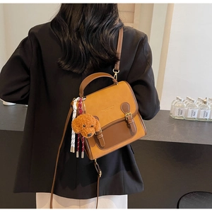 Detail of a brown leather crossbody bag featuring a cute puppy plush charm and metal buckles