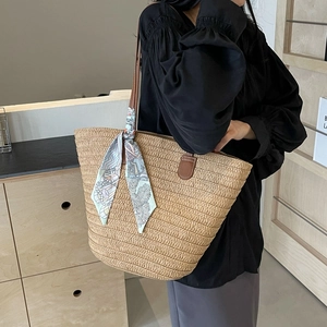 Large straw tote bag with brown leather handles and blue scarf on a model's shoulder